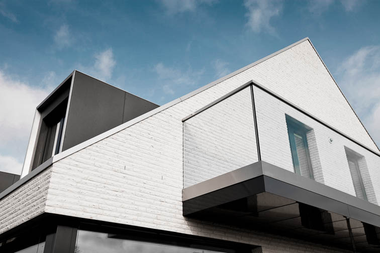 Außenaufnahme Einfamilienhaus. Detail Balkon mit Glasbrüstung, weißem Klinker, grauer Dachgaube. Minimalistisch