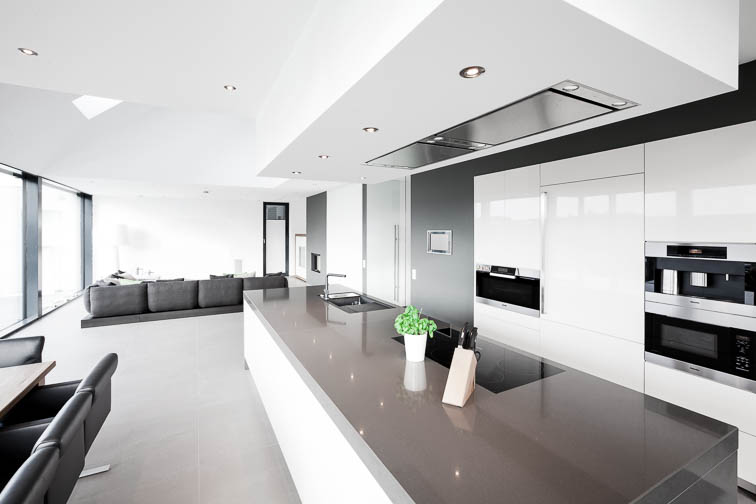 Innenraumperspektive eines Küchenblocks mit Couch im Hintergrund. Minimalistisch, weiß, grau. Einfamilienhaus in Telgte